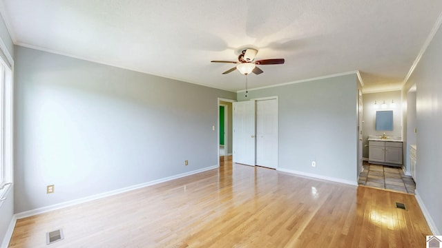 unfurnished bedroom featuring light wood-style flooring, baseboards, ensuite bath, crown molding, and a closet