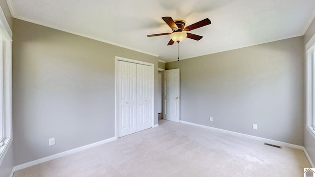 unfurnished bedroom featuring baseboards, light colored carpet, a closet, crown molding, and ceiling fan