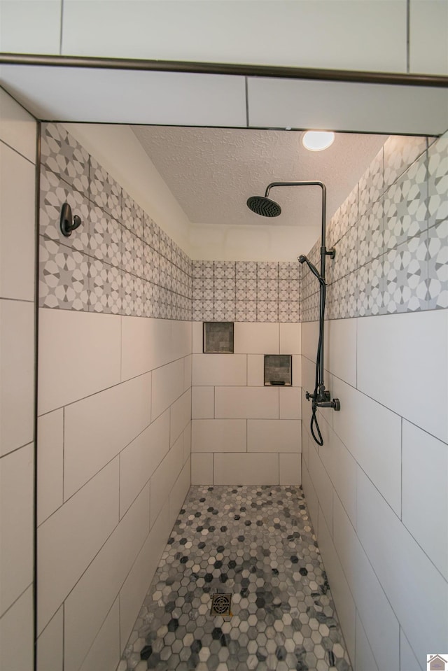 full bathroom with tiled shower, a textured ceiling, and tile walls