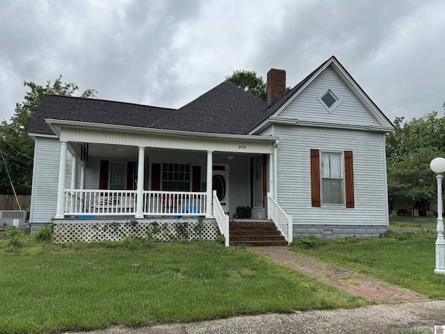 bungalow-style home featuring a porch, a chimney, a front yard, central air condition unit, and roof with shingles