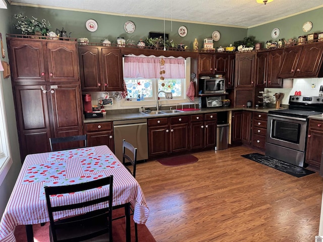 kitchen featuring appliances with stainless steel finishes, a sink, crown molding, light wood-style flooring, and a textured ceiling
