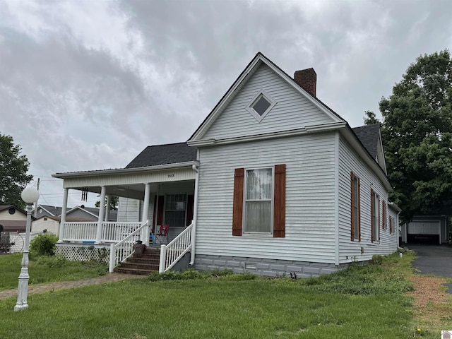 view of front facade with a porch, a chimney, a front yard, and roof with shingles