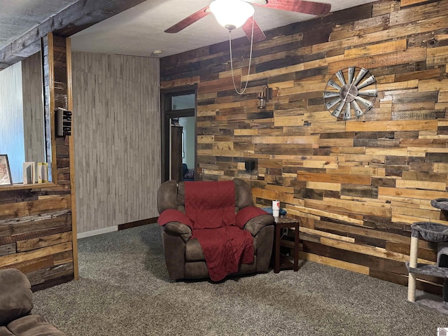 sitting room with wooden walls, carpet, a ceiling fan, and baseboards