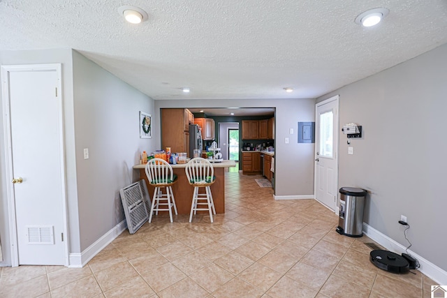 157 Calvert Dr, Paducah, KY 42003 - kitchen with a peninsula, brown cabinetry, a textured ceiling, a kitchen bar, and freestanding refrigerator