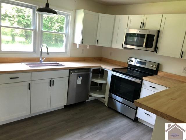 181 W 3rd St, Calvert City, KY 42029 - kitchen featuring appliances with stainless steel finishes, a sink, white cabinetry, wood finished floors, and decorative light fixtures