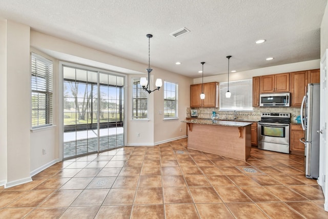 kitchen featuring appliances with stainless steel finishes, decorative light fixtures, a breakfast bar area, backsplash, and a center island