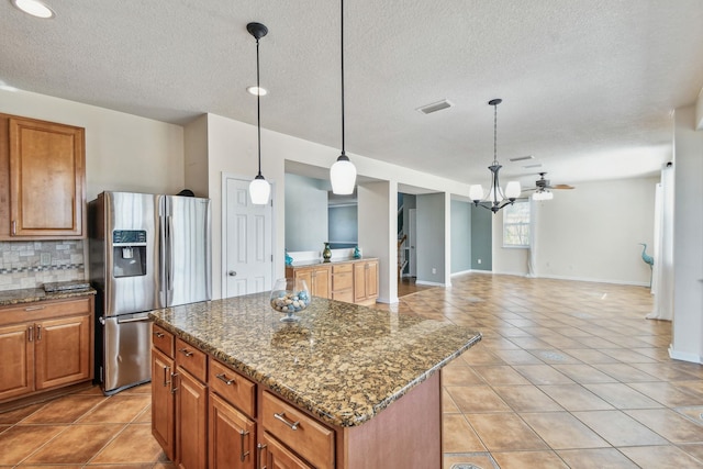 kitchen with pendant lighting, dark stone countertops, a center island, tasteful backsplash, and stainless steel fridge with ice dispenser