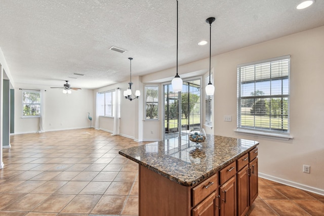 kitchen featuring a kitchen island, dark stone countertops, light tile patterned floors, and decorative light fixtures