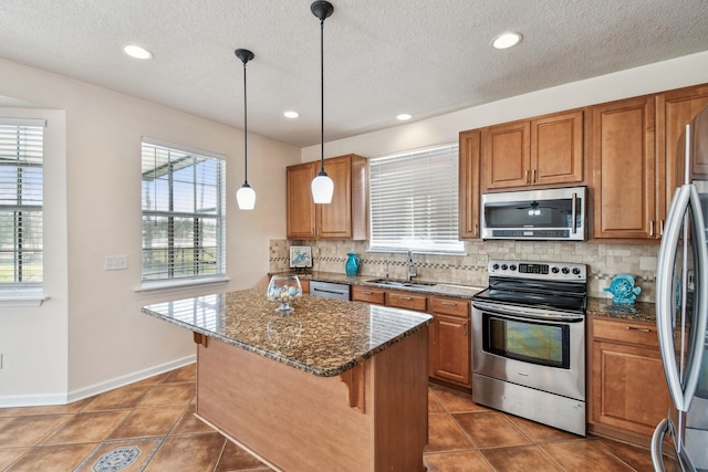 kitchen featuring sink, appliances with stainless steel finishes, a kitchen breakfast bar, pendant lighting, and dark stone counters