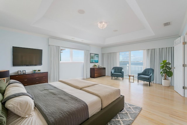 bedroom with a tray ceiling, multiple windows, and light hardwood / wood-style floors