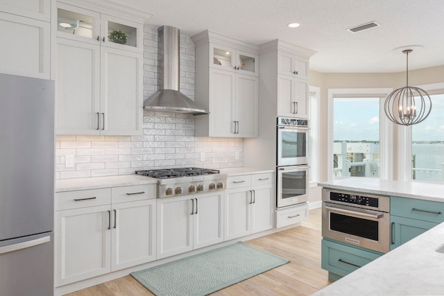 kitchen with white cabinetry, wall chimney exhaust hood, tasteful backsplash, light hardwood / wood-style flooring, and appliances with stainless steel finishes