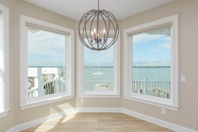 unfurnished dining area with light hardwood / wood-style floors, a water view, and a chandelier