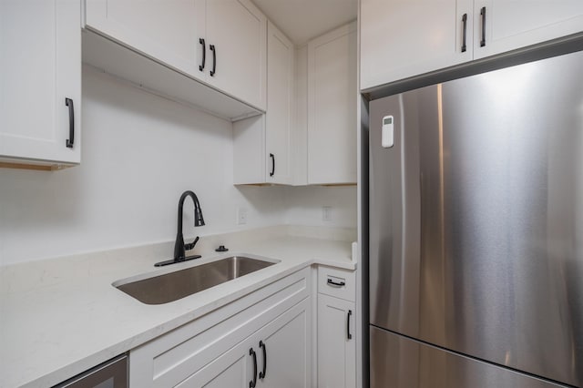 kitchen featuring white cabinetry, sink, light stone counters, and stainless steel fridge