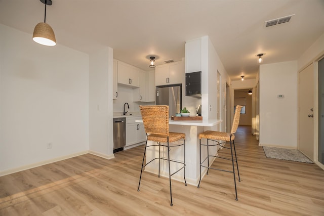 kitchen featuring white cabinetry, stainless steel appliances, a breakfast bar area, and pendant lighting