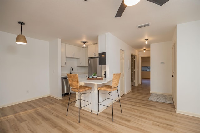 kitchen with a kitchen bar, light hardwood / wood-style flooring, kitchen peninsula, stainless steel appliances, and white cabinets