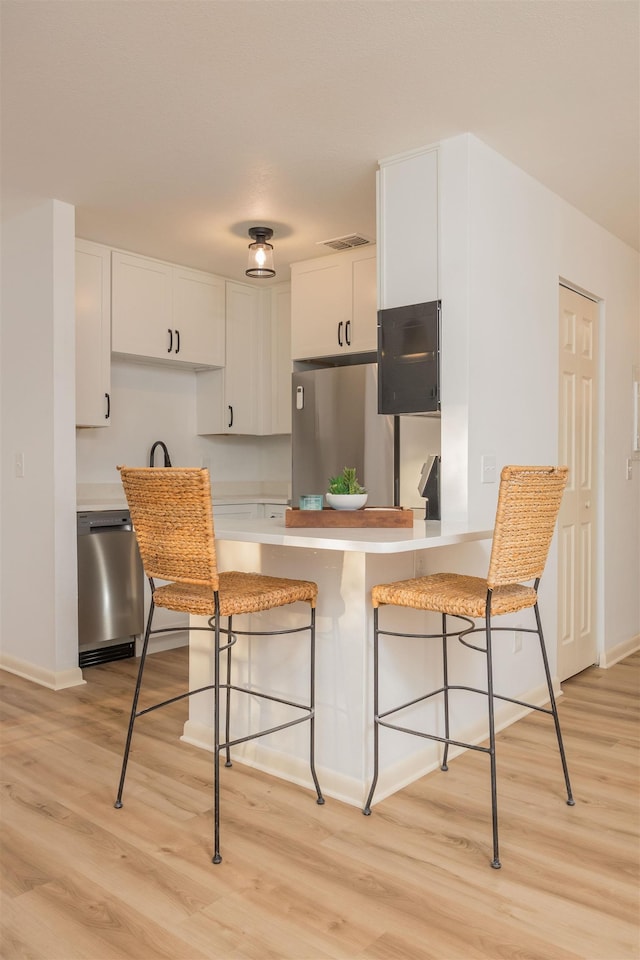 kitchen featuring a breakfast bar, light hardwood / wood-style flooring, appliances with stainless steel finishes, kitchen peninsula, and white cabinets