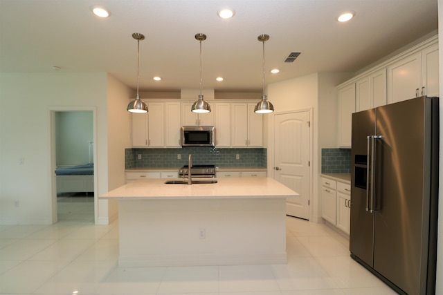 kitchen with a kitchen island with sink, white cabinets, sink, appliances with stainless steel finishes, and decorative light fixtures