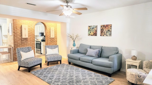 living room with ceiling fan, light hardwood / wood-style floors, and brick wall