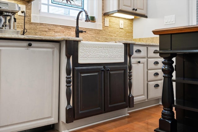 details with light stone countertops, backsplash, sink, light hardwood / wood-style floors, and white cabinetry