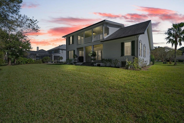 back house at dusk featuring a lawn, ceiling fan, a balcony, and central air condition unit