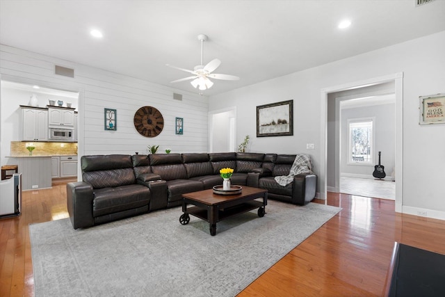 living room featuring wood walls, ceiling fan, and light wood-type flooring