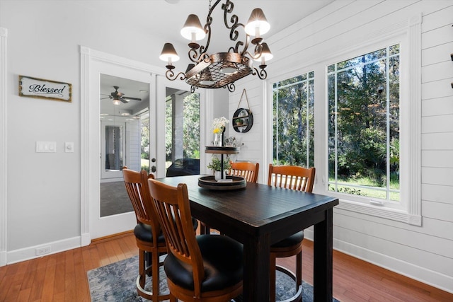 dining area with ceiling fan with notable chandelier, wooden walls, and dark wood-type flooring