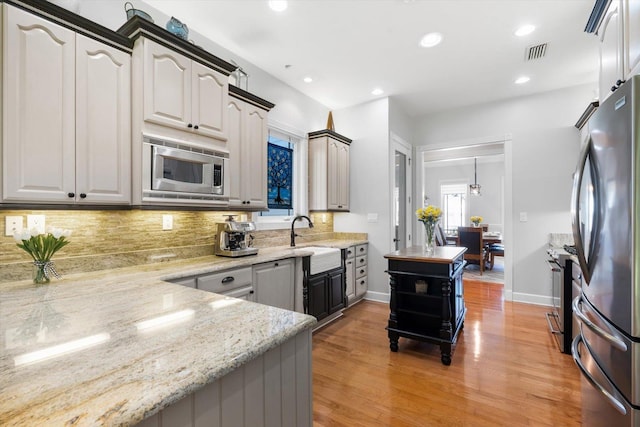 kitchen featuring sink, stainless steel appliances, a barn door, light stone counters, and light hardwood / wood-style flooring