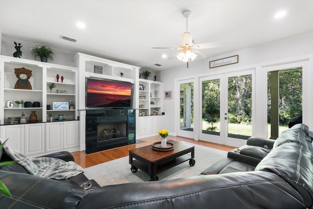 living room featuring ceiling fan, light wood-type flooring, a fireplace, and french doors