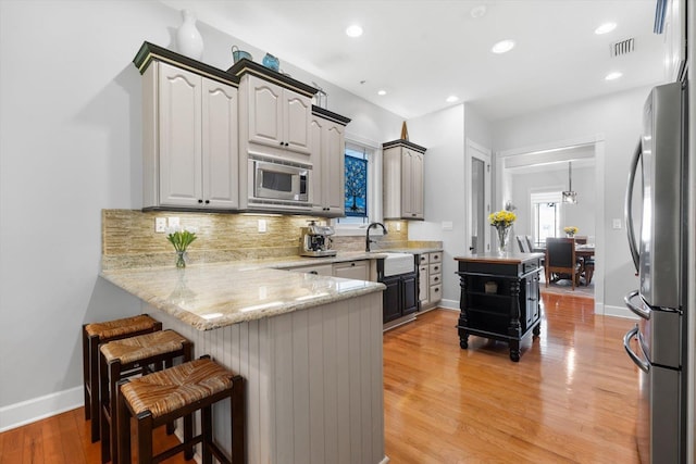 kitchen featuring gray cabinetry, backsplash, appliances with stainless steel finishes, light hardwood / wood-style floors, and kitchen peninsula