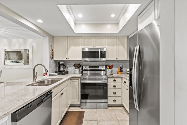 kitchen featuring sink, appliances with stainless steel finishes, a tray ceiling, light stone countertops, and decorative backsplash