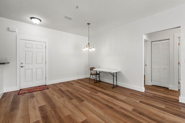 interior space featuring a textured ceiling, a notable chandelier, dark wood-type flooring, visible vents, and baseboards