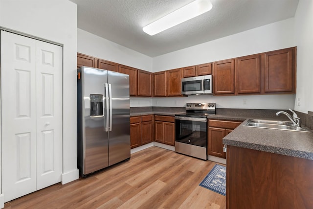 kitchen featuring stainless steel appliances, dark countertops, a sink, a textured ceiling, and light wood-type flooring