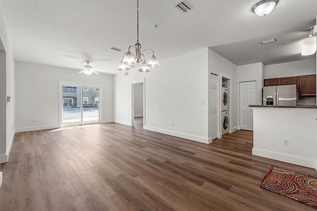 unfurnished living room featuring stacked washer and clothes dryer, visible vents, dark wood-type flooring, a textured ceiling, and baseboards