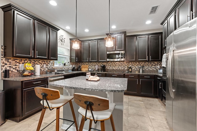 kitchen featuring appliances with stainless steel finishes, a kitchen breakfast bar, light stone counters, decorative light fixtures, and a kitchen island