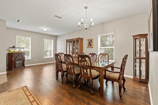 dining space featuring dark wood-type flooring, a textured ceiling, and a notable chandelier