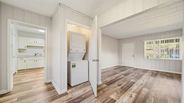 washroom with crown molding, stacked washing maching and dryer, sink, and light hardwood / wood-style floors