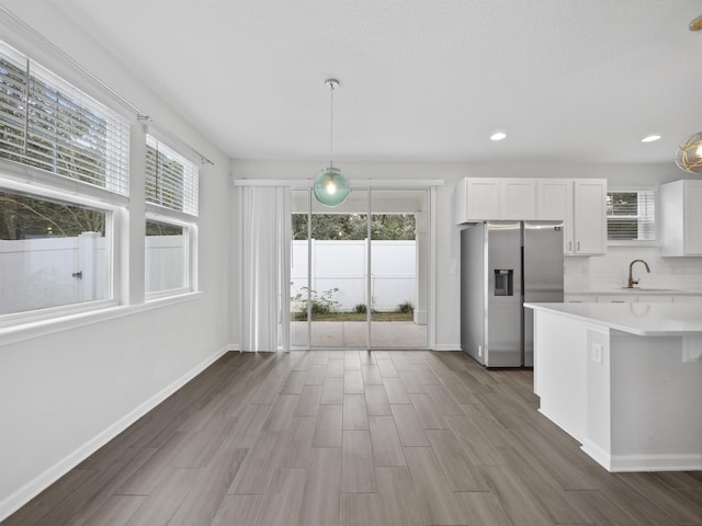 kitchen with stainless steel fridge with ice dispenser, plenty of natural light, white cabinets, and pendant lighting