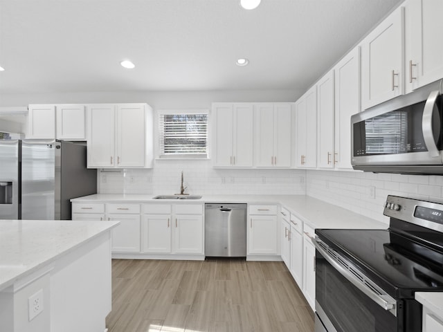 kitchen with light stone countertops, white cabinetry, sink, light hardwood / wood-style flooring, and appliances with stainless steel finishes