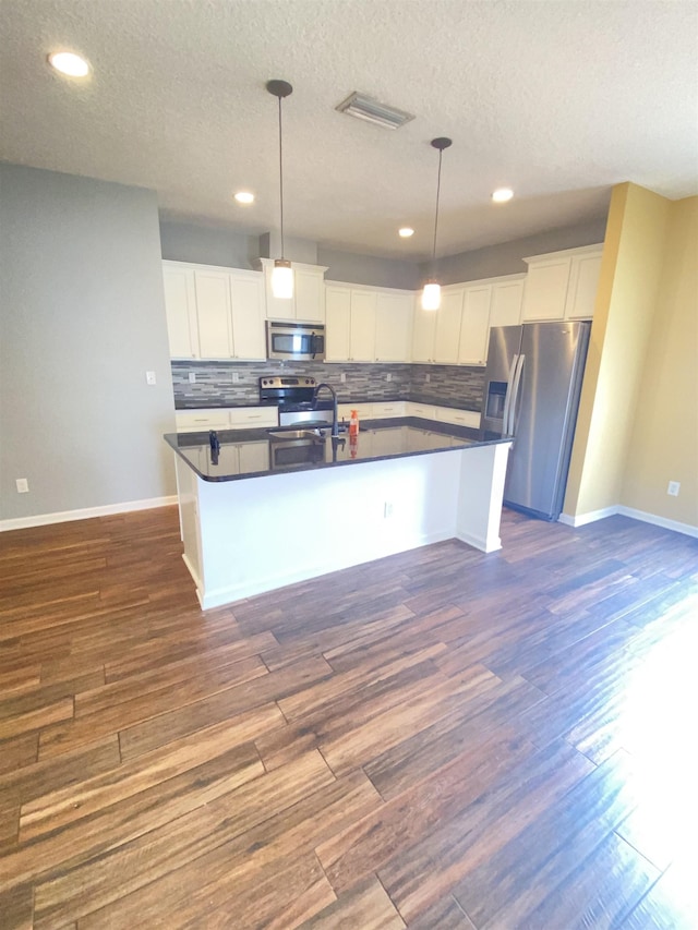 kitchen featuring white cabinets, decorative light fixtures, a kitchen island with sink, and appliances with stainless steel finishes