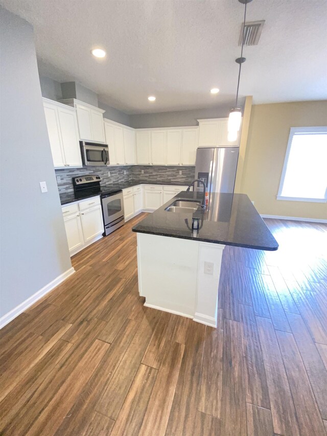 kitchen with stainless steel appliances, sink, a center island with sink, white cabinets, and hanging light fixtures