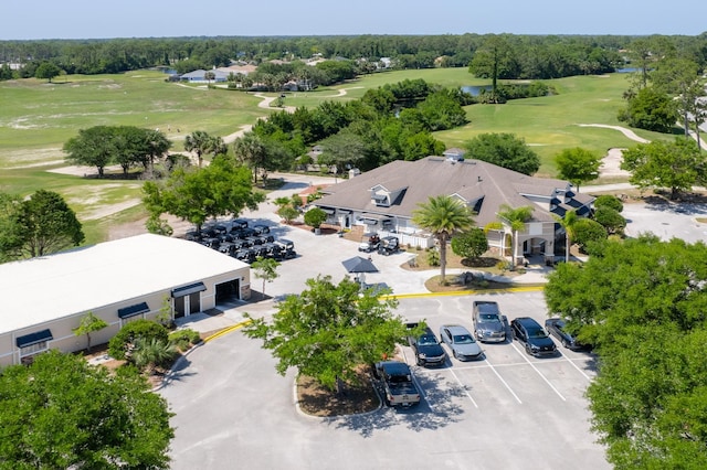 drone / aerial view of a golf club, a tree filled landscape, and a nearby body of water