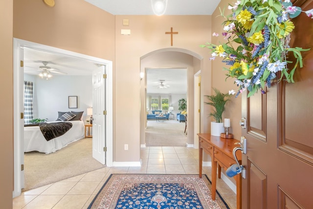 entrance foyer with light carpet, ceiling fan, light tile patterned floors, arched walkways, and baseboards