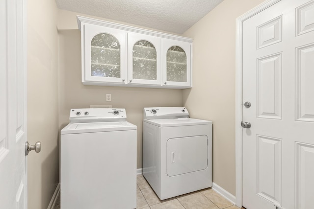 clothes washing area featuring washer and clothes dryer, light tile patterned floors, a textured ceiling, and baseboards