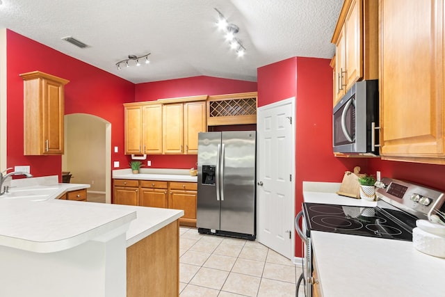kitchen with stainless steel appliances, a sink, track lighting, light countertops, and a peninsula
