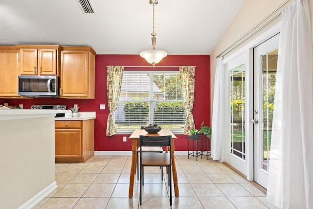 kitchen featuring stainless steel microwave, decorative light fixtures, light countertops, baseboards, and brown cabinetry