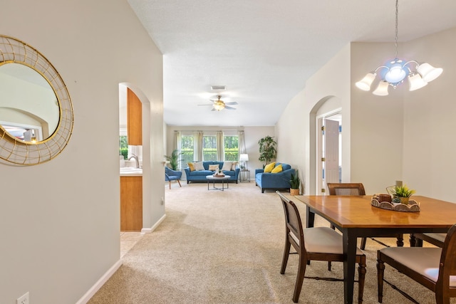 dining room with arched walkways, light colored carpet, a chandelier, and ceiling fan