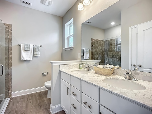 bathroom featuring a shower stall, wood finished floors, baseboards, and double vanity