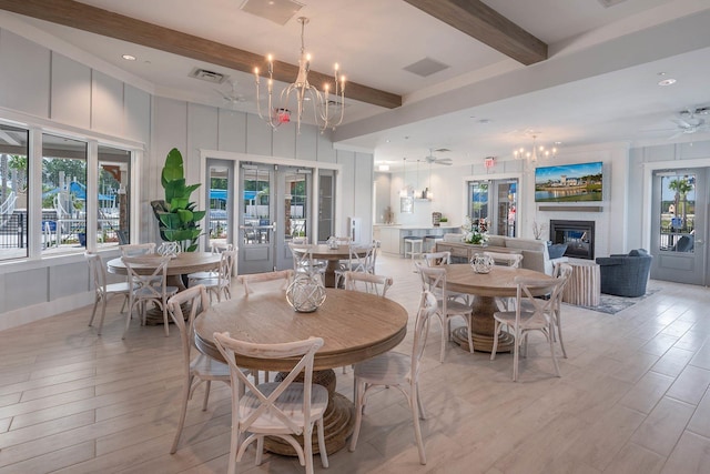 dining area featuring beamed ceiling, a glass covered fireplace, ceiling fan, a chandelier, and light wood-style flooring