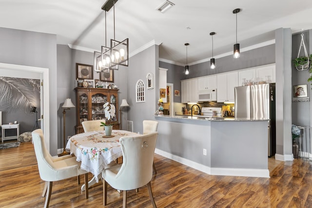 dining area with a notable chandelier, sink, ornamental molding, and dark wood-type flooring