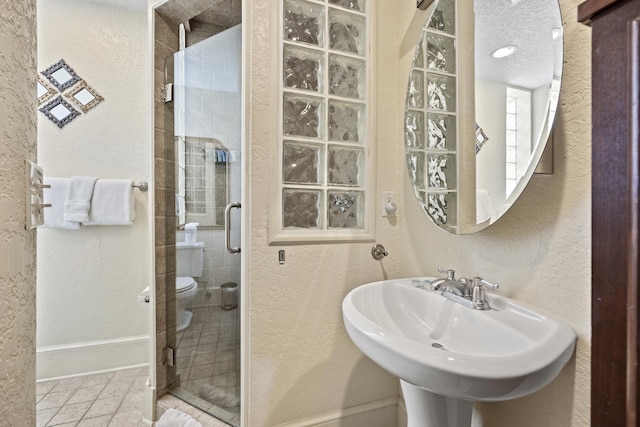 bathroom featuring a textured ceiling, toilet, a shower with door, and sink